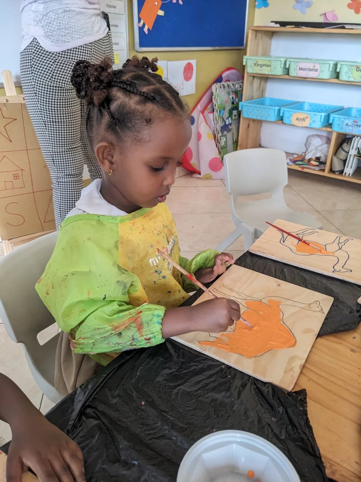 A child in a paint apron painting at an Eco-Bloom classroom table
